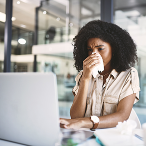 woman blowing nose in tissue at desk