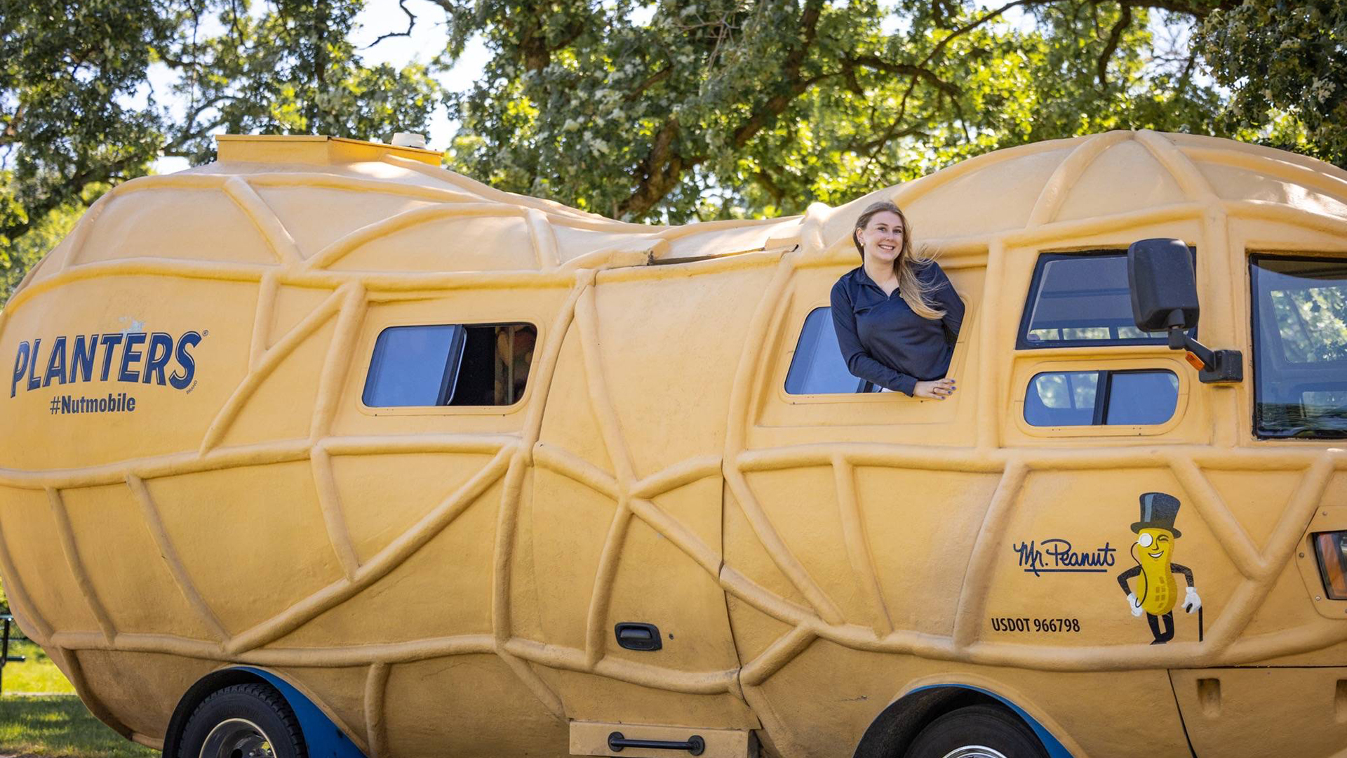 A person leaning out the Planters Nutmobile, a peanut-shaped promotional vehicle.