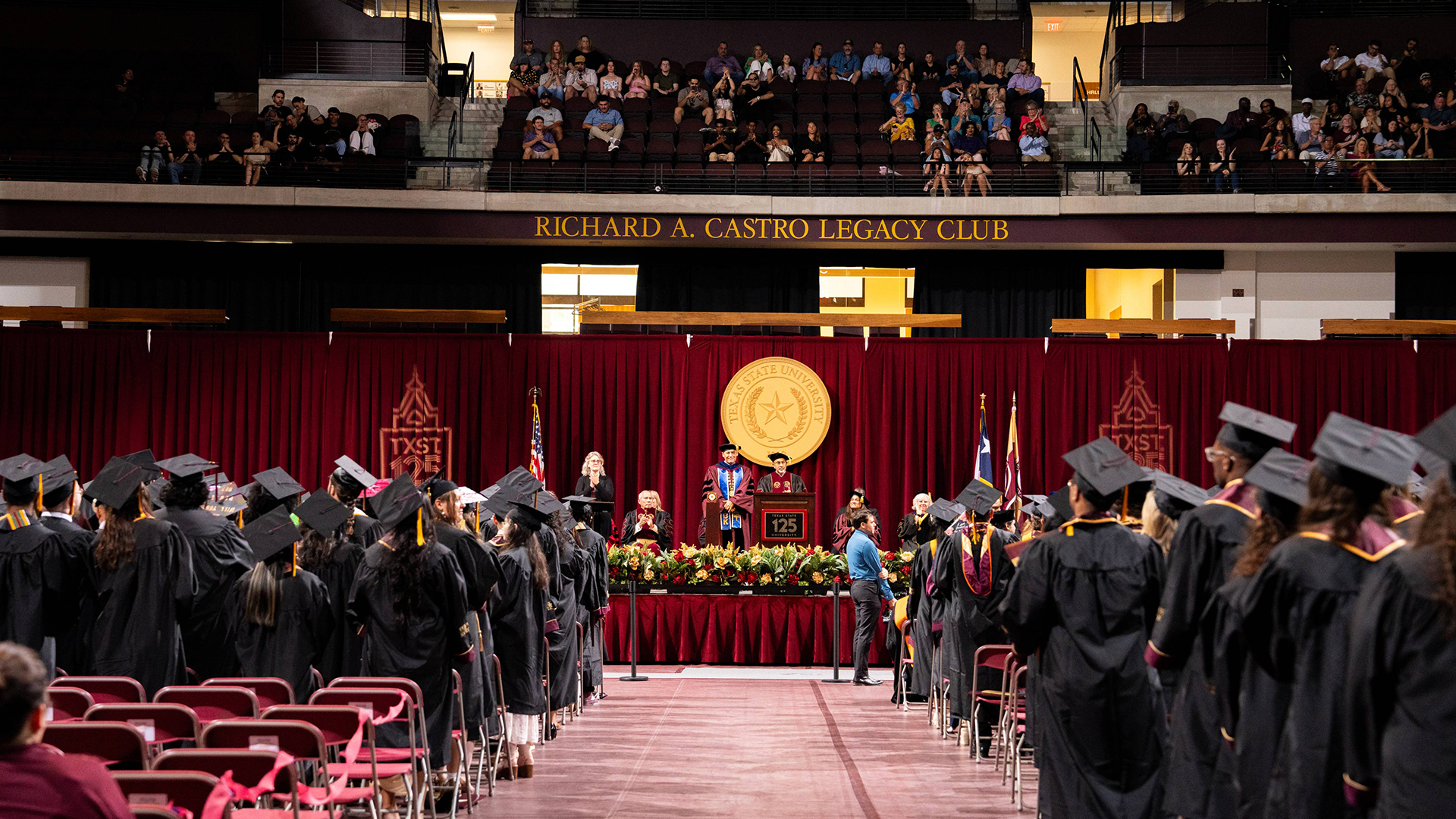 Graduates in caps and gowns attend a Texas State University commencement ceremony.