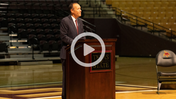 man behind podium speaking to crowd with YouTube play button on top directing to video