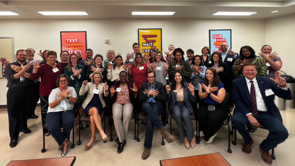 ACC and TXST team members in group meeting holding up hand signs for schools