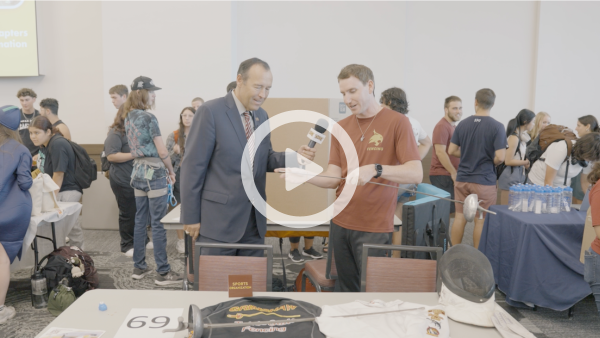 man and student talking at student org fair with play button