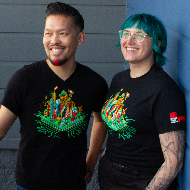 Two smiling people wearing a green EFF 35th Anniversary digital cityscape on a black shirt.