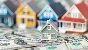 A row of small model houses sit on top of a pile of US cash