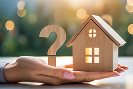 An outstretched hand holds a small wooden house with a question mark next to it