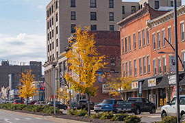 A downtown street in Olean, New York, is lined with small businesses in historical buildings with cars parked out front