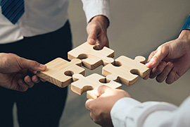 Four people standing in a circle each hold a puzzle piece