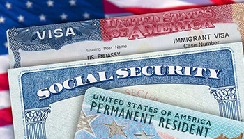 An immigrant Visa card, Social Security card, and permanent resident/green card sit atop a US flag