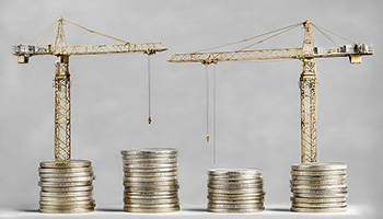 Two construction cranes sit atop stacks of coins