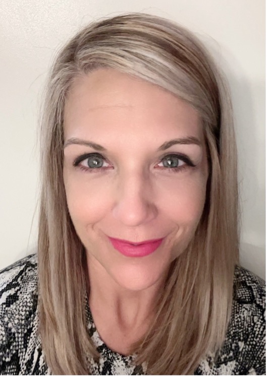 A portrait of Carrinna Caldwell smiling. Carrinna has light colored hair and blue eyes and is wearing pink lipstick and a black and white top.