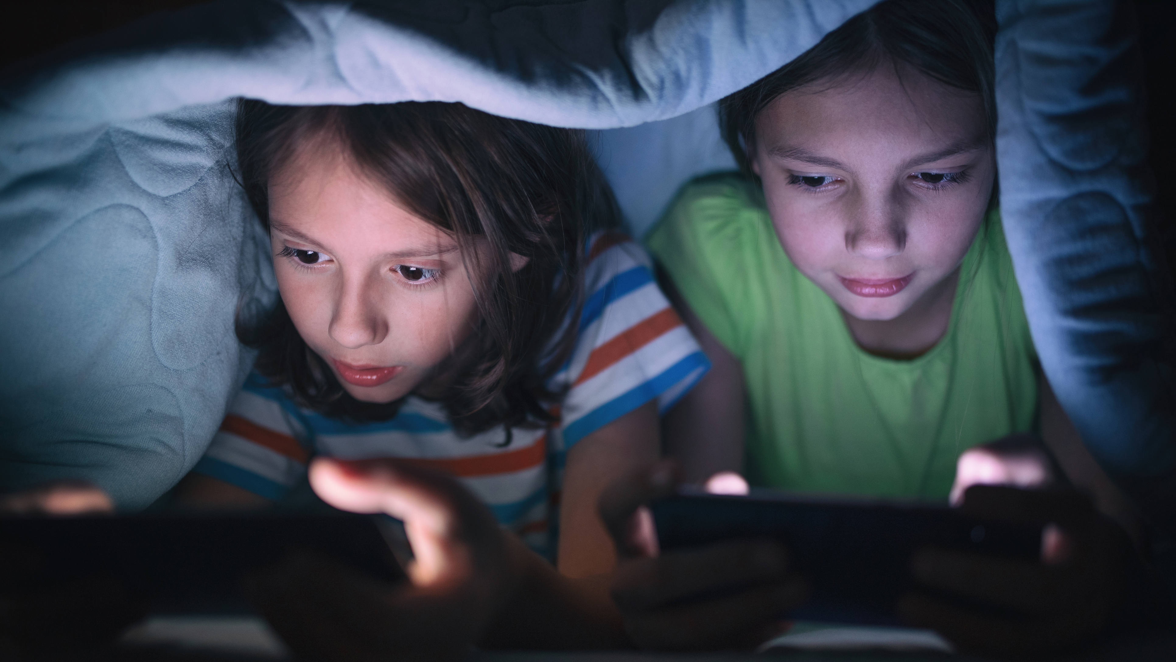2 girls using tablets under covers
