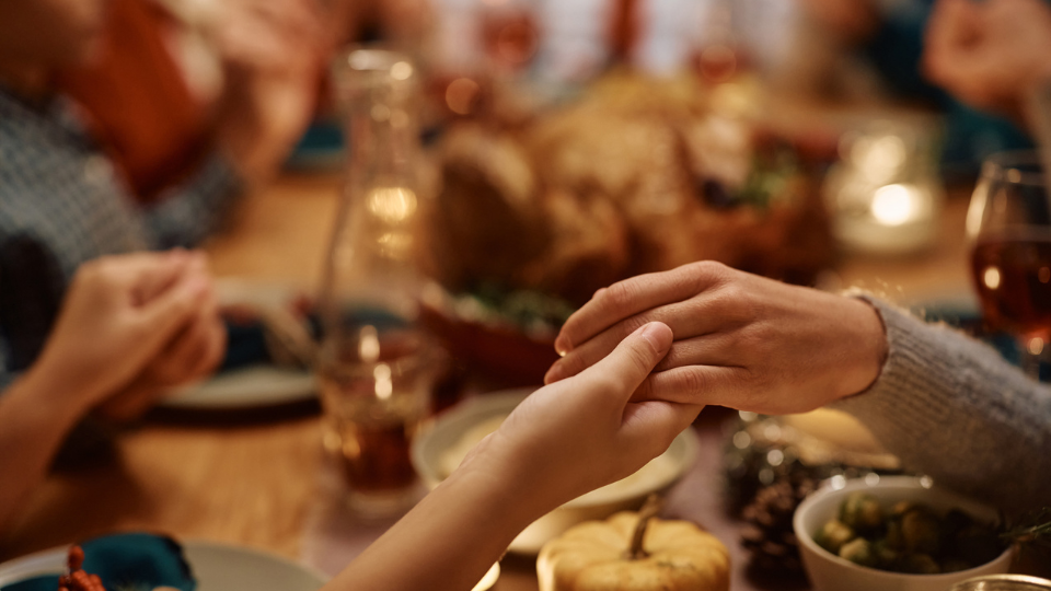 Close up of people holding hands around a blurred Thanksgiving table